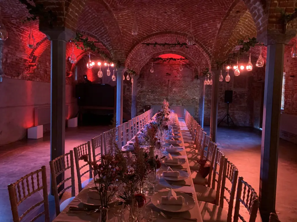 Lange feesttafel in een gewelfde bakstenen kelder met rode sfeerverlichting
