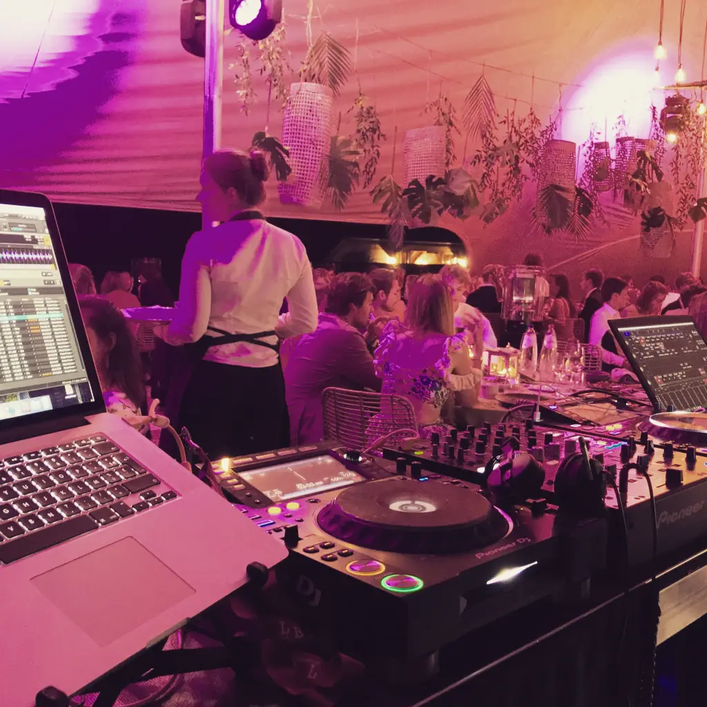 Zicht vanachter de DJ-booth op een tentfeest met roze sfeerverlichting