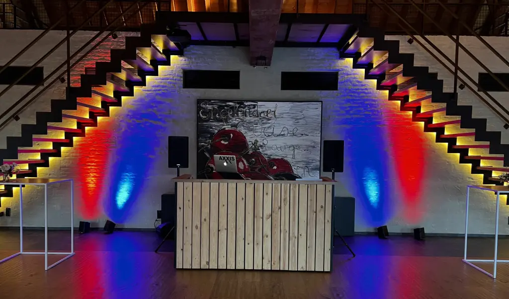 Houten DJ-booth met speakers en gekleurde uplighters in een loft